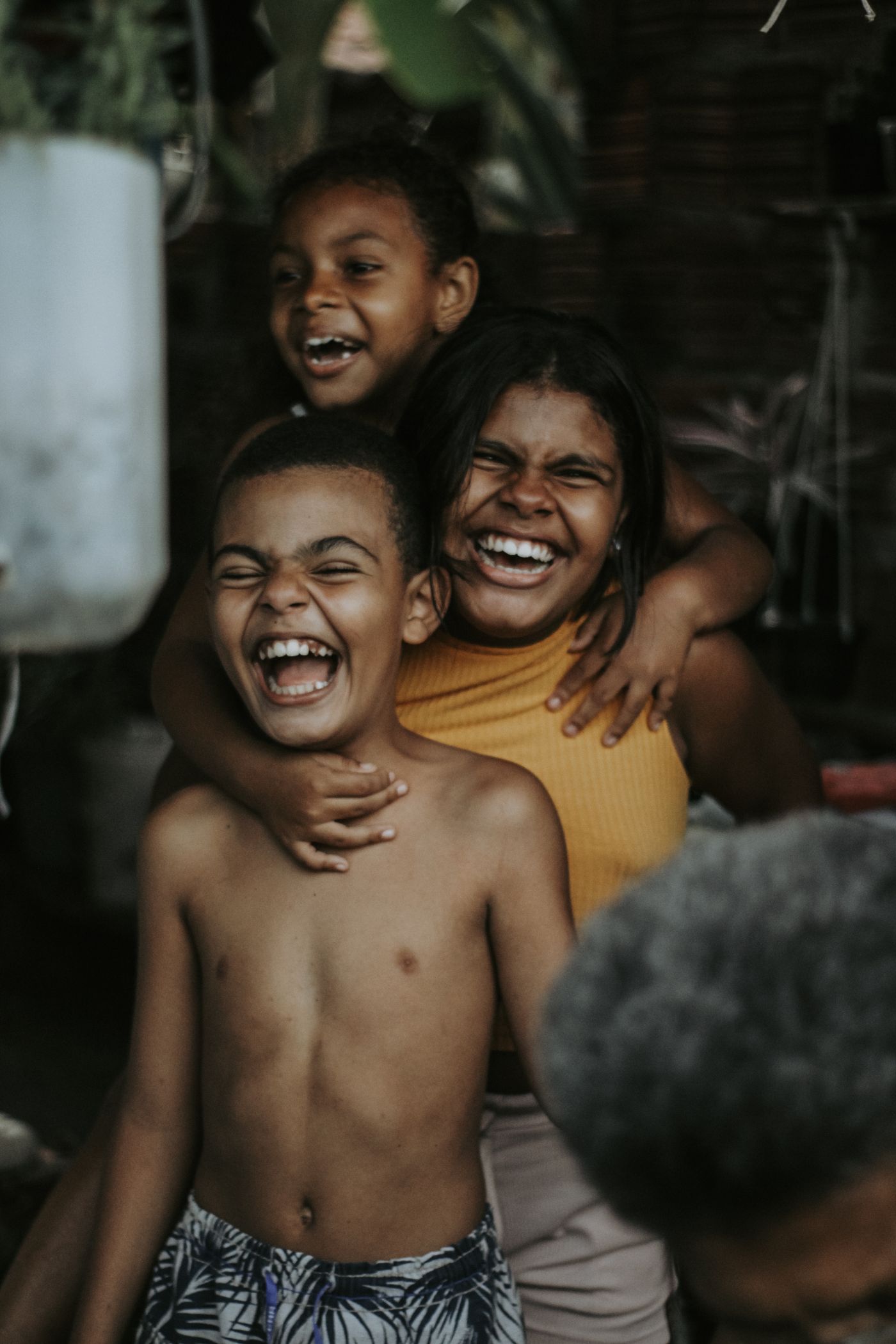 A real reference photograph: three children piled in an impromptu piggyback stack, all mid-laugh, on a porch